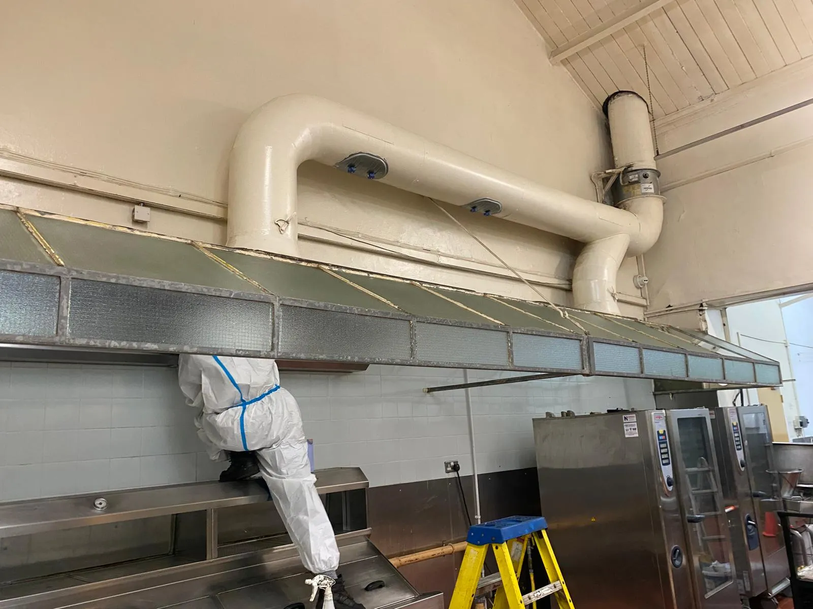 Rams technician in full PPE cleaning a stainless kitchen canopy